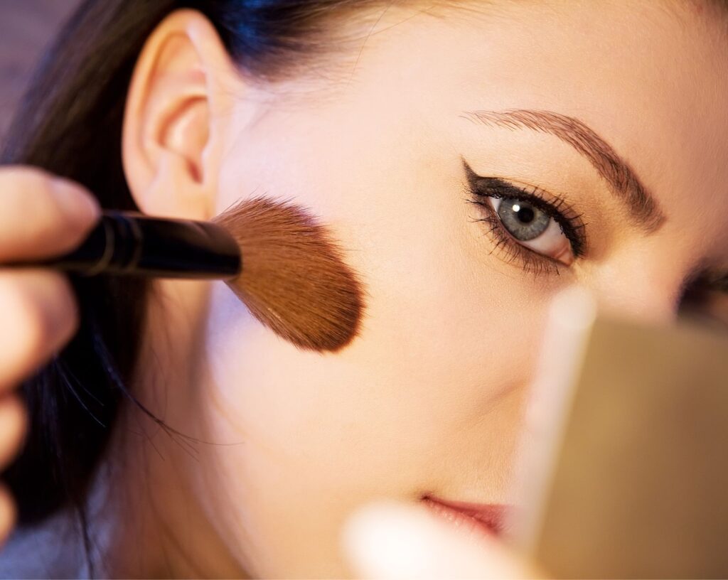 Finished sharp winged eyeliner, with a blush brush sweeping across the cheek