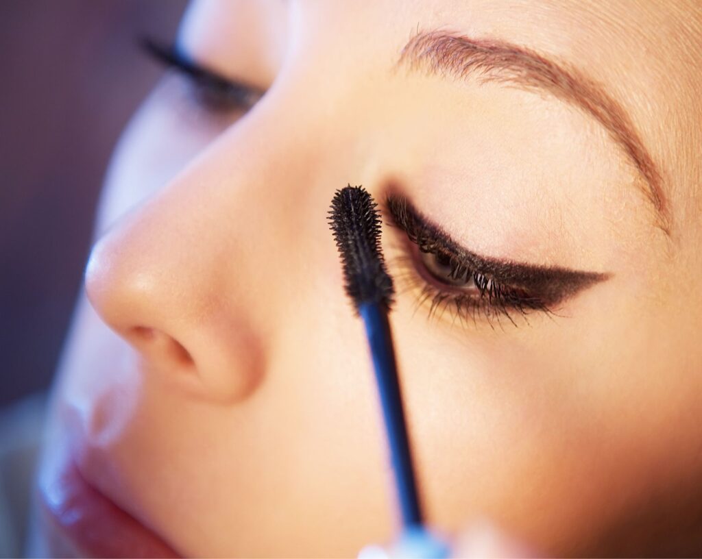 Applying black mascara to the lashes over a finished winged eyeliner look